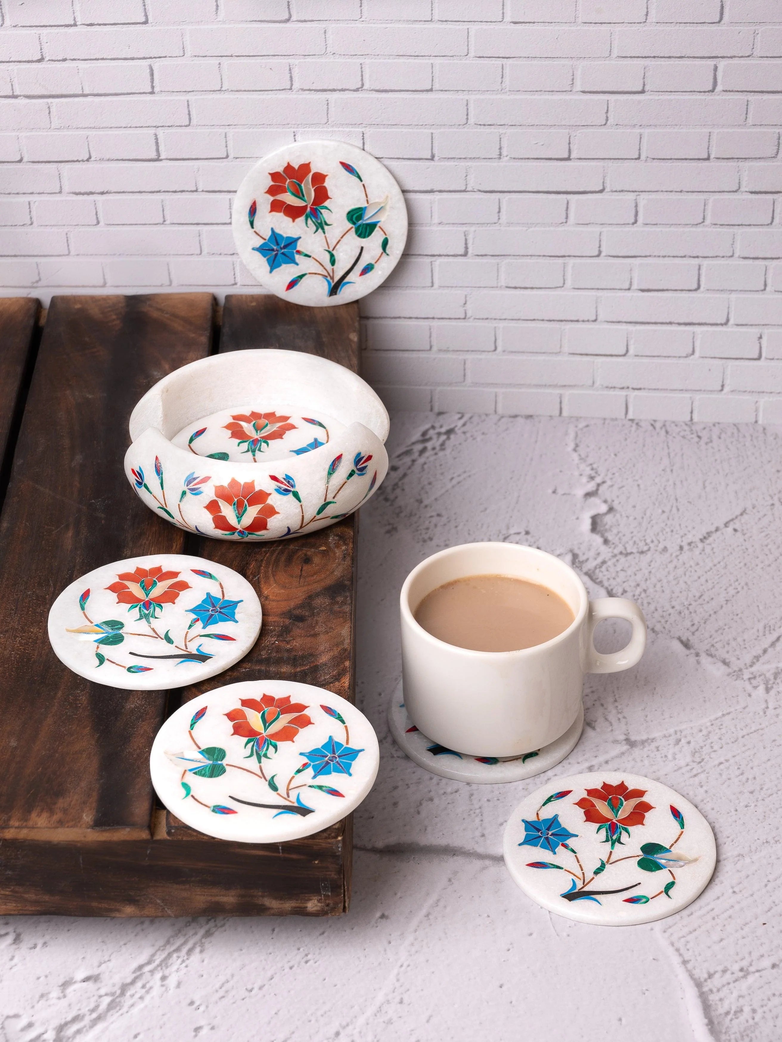 Floral coasters on a table with a cup of coffee against a white brick wall.