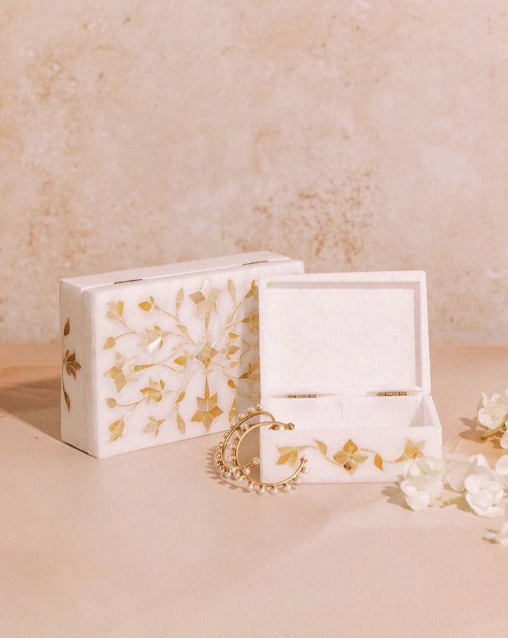 White jewelry box with gold floral patterns on a beige surface